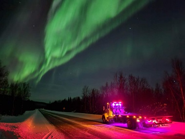 roadside assistance truck driving at night under green aurora borealis lights