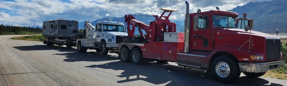 JC's Towing and Recovery LLC red tow truck towing a tow truck that is towing a camper